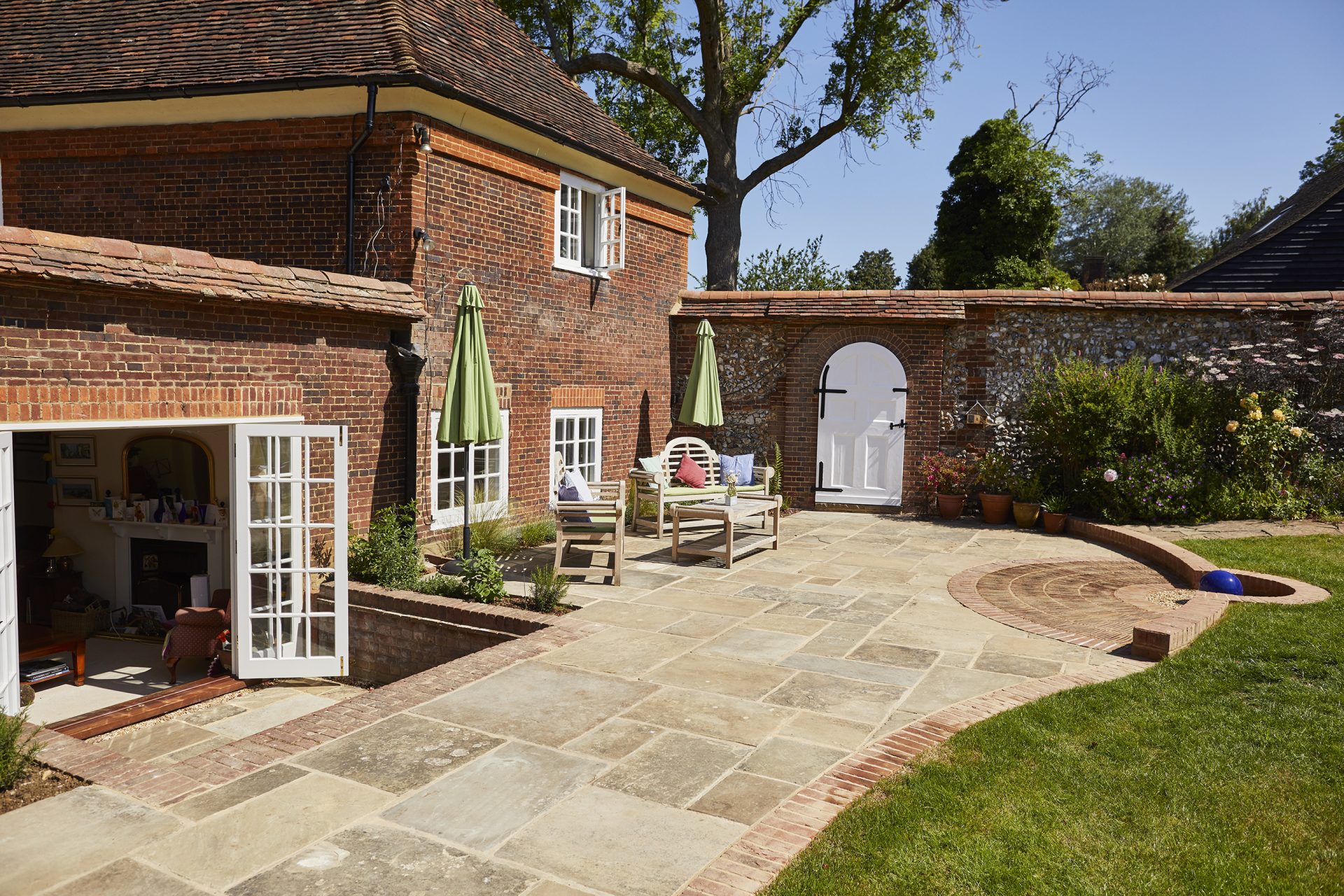 Stone-paved courtyard with outdoor seating, brick-edged lawn and a traditional red-brick house.