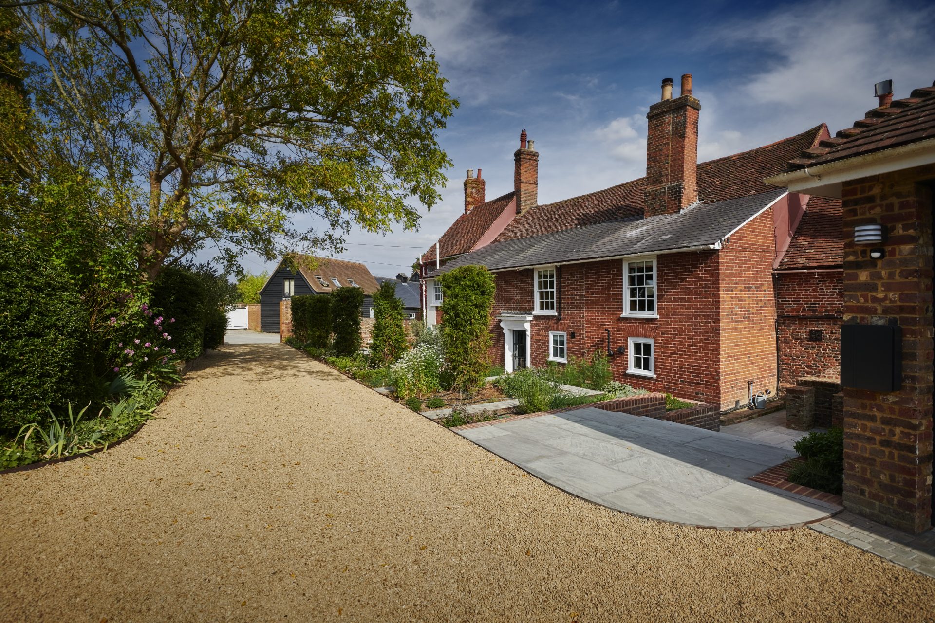 Gravel driveway beside a traditional red-brick house, with stone paving and landscaped planting borders.
