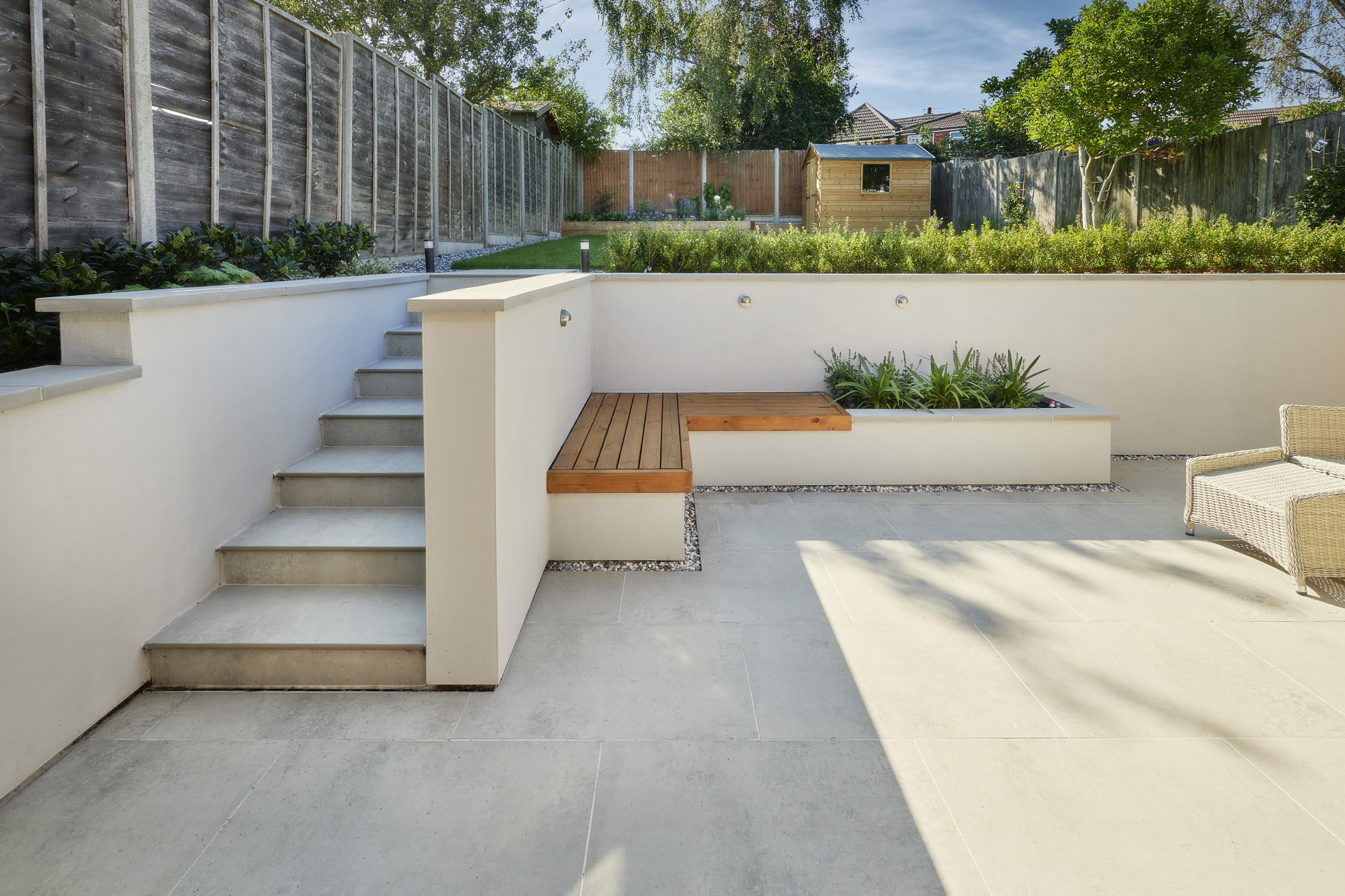 Contemporary porcelain patio with built-in rendered seating, timber bench details and landscaped planting.