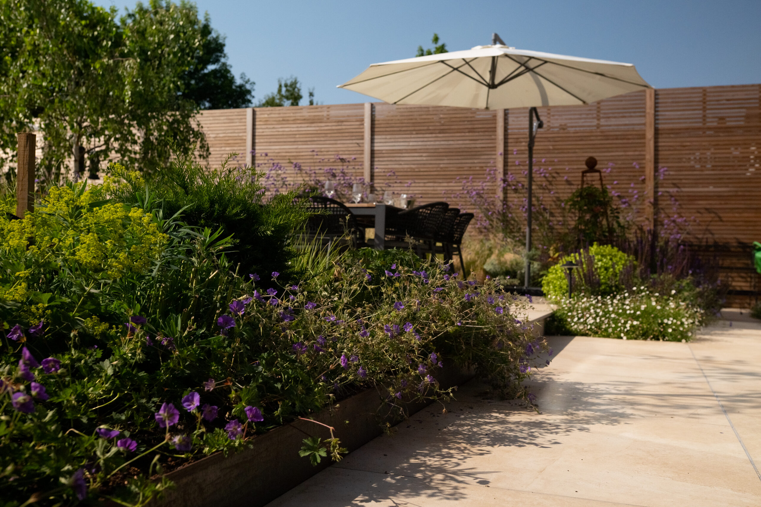 Horizontal timber privacy fencing surrounding a landscaped patio garden with outdoor dining area and planting.