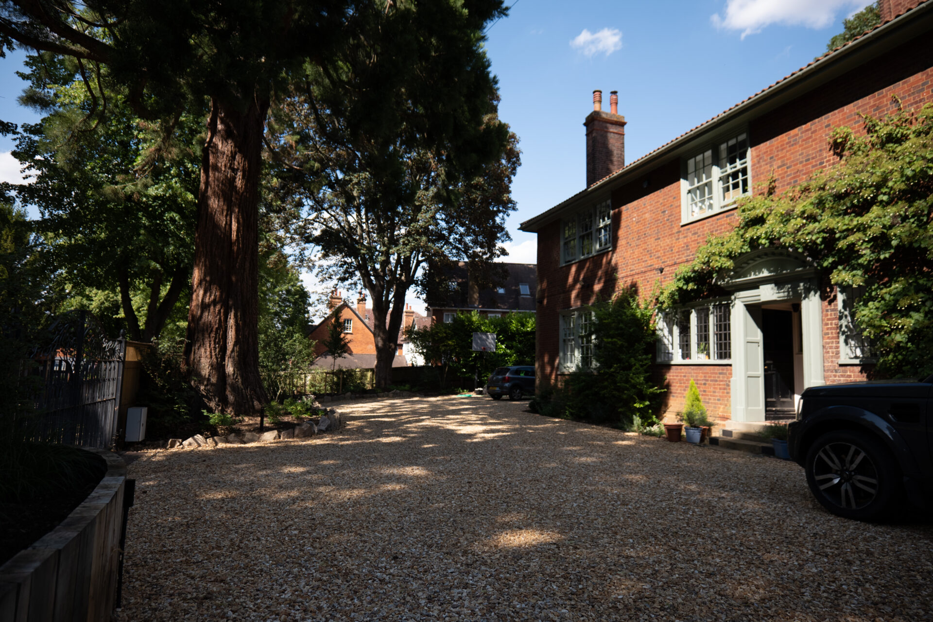 Large gravel driveway landscaped around mature trees in front of a brick home.