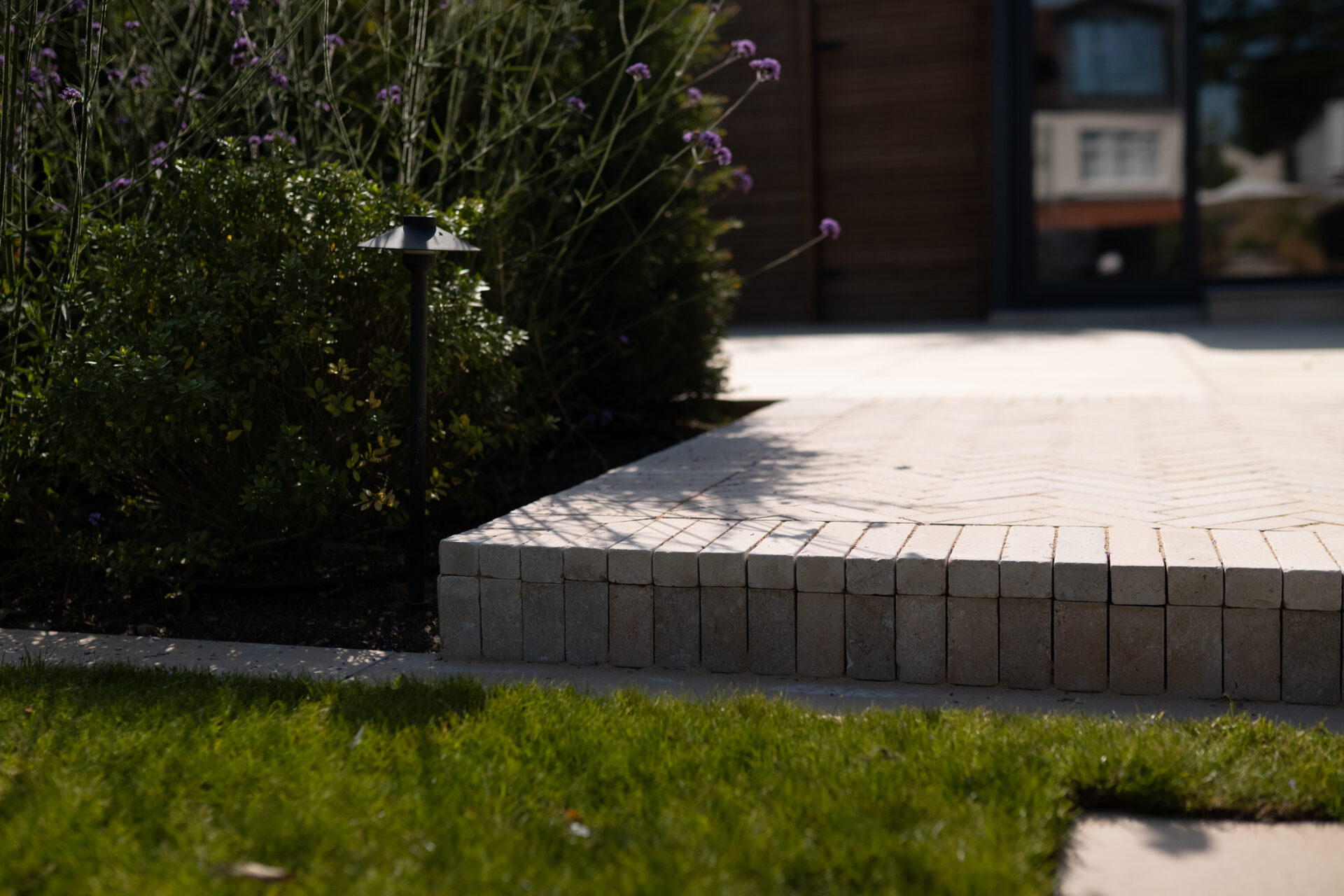 Modern paved garden edge with neat block detailing, planting and integrated garden lighting.