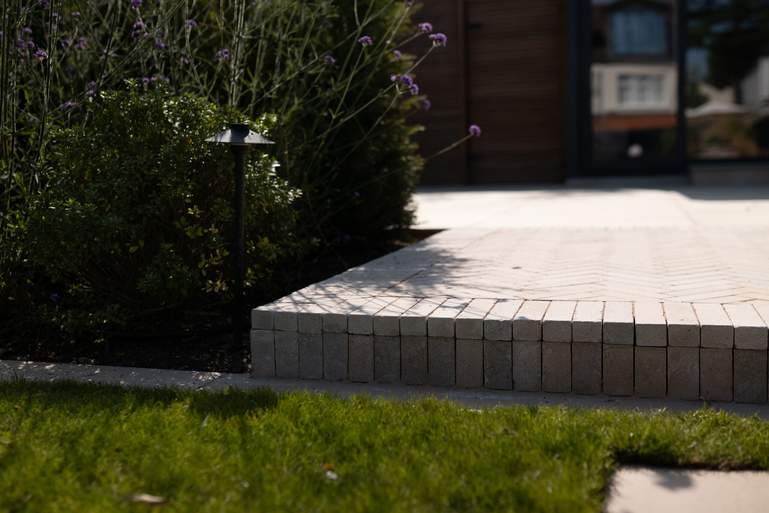 Modern paved garden edge with neat block detailing, planting and integrated garden lighting.