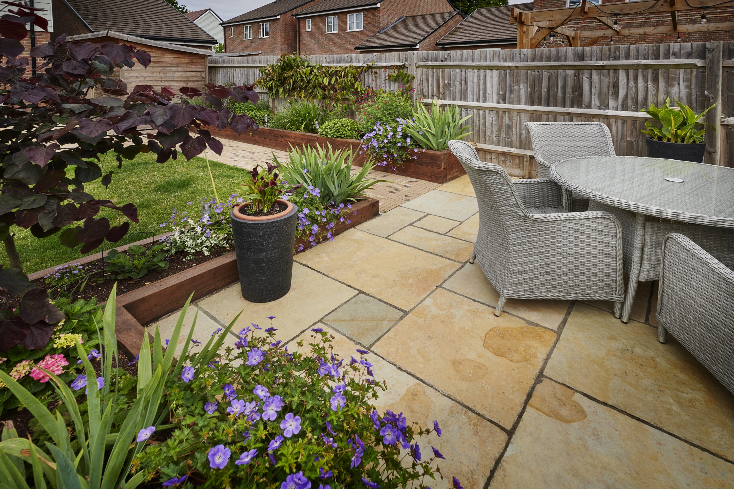 Small garden design with natural stone patio, outdoor seating, raised timber planting beds and colourful planting.